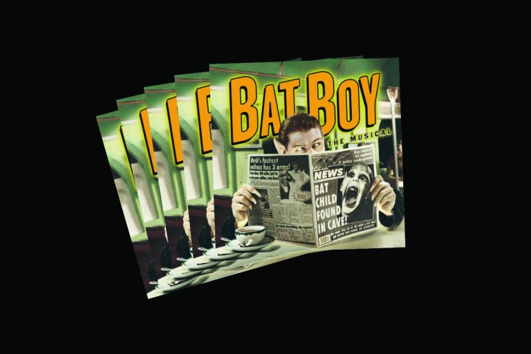 Stack of Bat Boy the Musical programs featuring man reading newspaper with BAT CHILD FOUND IN CAVE headline