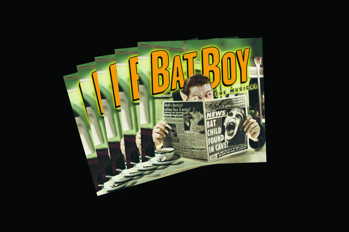 Stack of Bat Boy the Musical programs featuring man reading newspaper with BAT CHILD FOUND IN CAVE headline