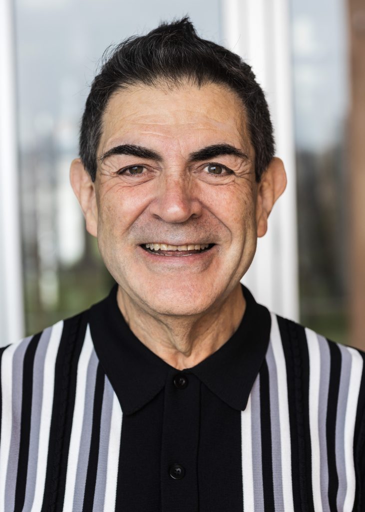 Man in black and white striped referee shirt smiling at camera in professional headshot photo