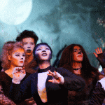 Group of diverse young people singing together passionately at concert or performance with dramatic stage lighting