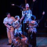 Theater performers in colorful costumes on stage during a live musical or dramatic performance with dramatic lighting