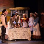 Theater performance with actors in period costumes gathered around a table on stage during dramatic scene