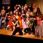 Theater cast in colorful period costumes posing together on stage after musical performance